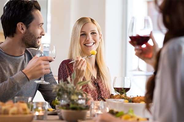 Drei Personen beim Abendessen mit einem Glas Rotwein in der Hand
